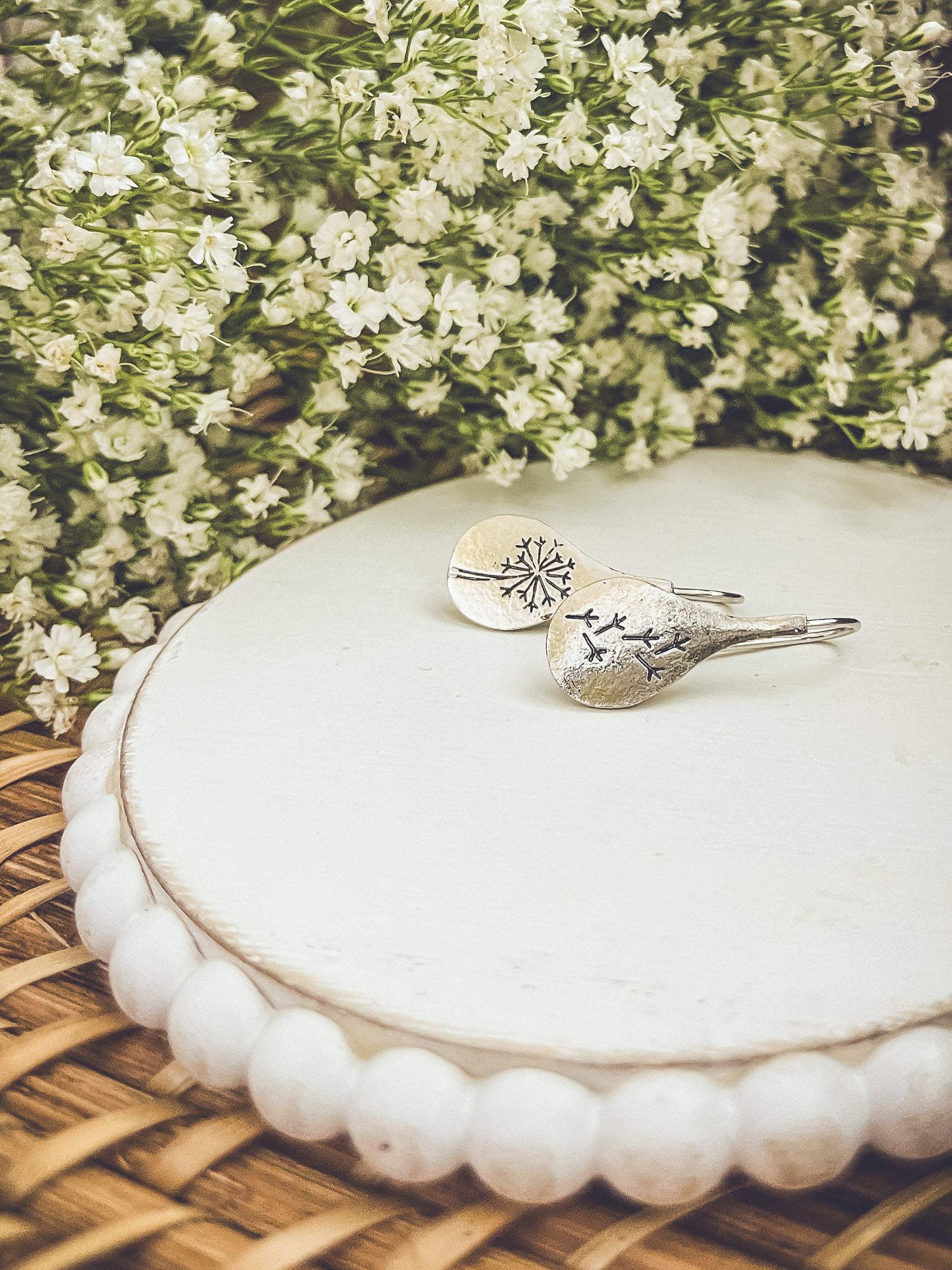 Silver earrings on a white round container with greenery in the background