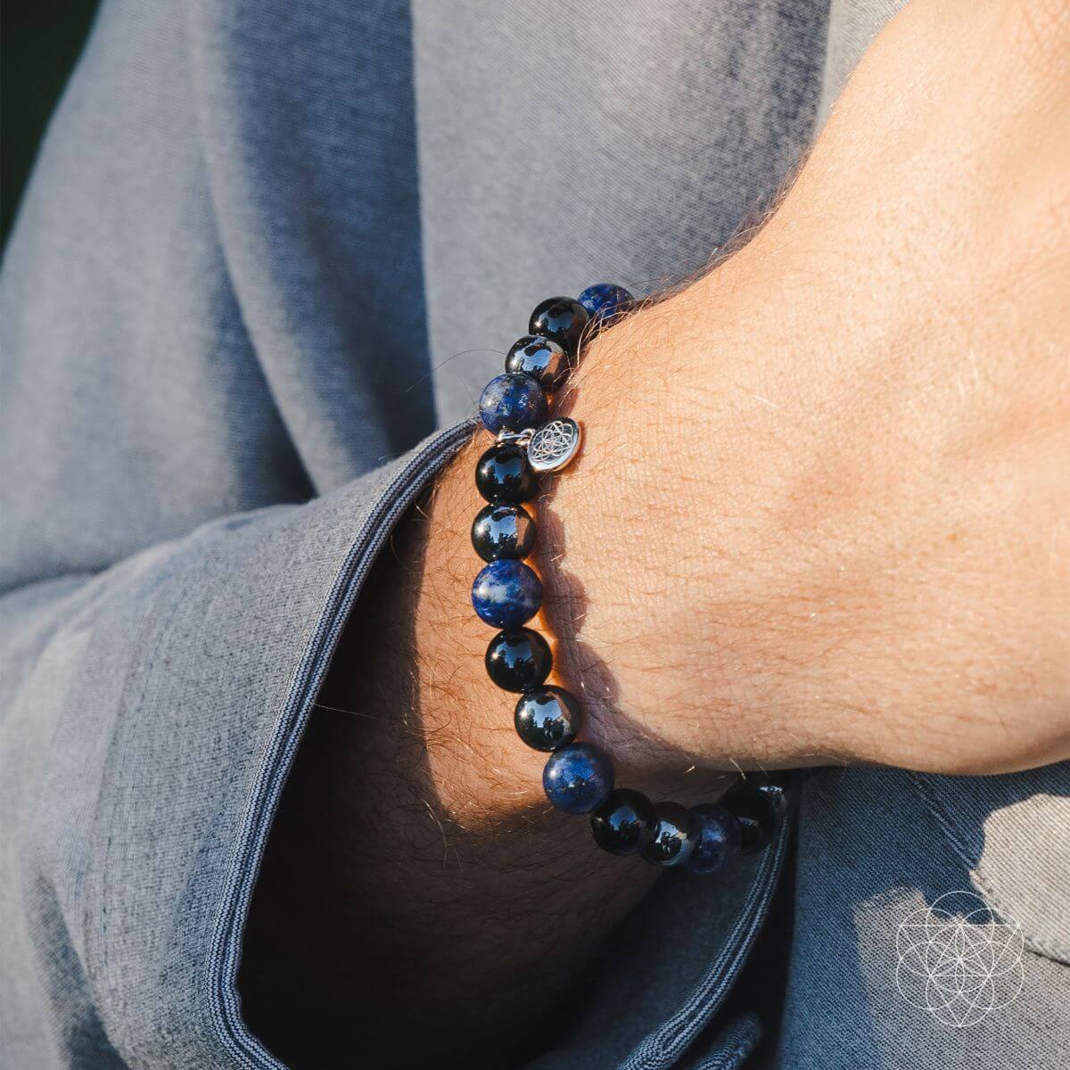 Close-up of a wrist wearing a blue beaded bracelet with a gray garment in the background